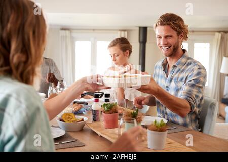 Young adult friends serving each other lunch at a dinner table, close up Stock Photo
