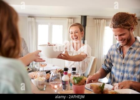 Young adult friends passing food across during lunch at a dinner table, close up Stock Photo
