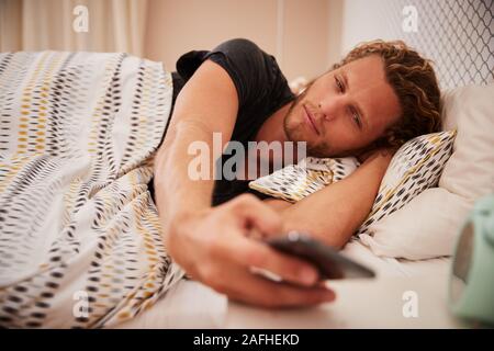 Millennial white man waking up in bad using smartphone, close up Stock Photo