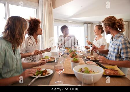 A group of millennial friends sitting at a table, eating lunch and talking, backlit Stock Photo