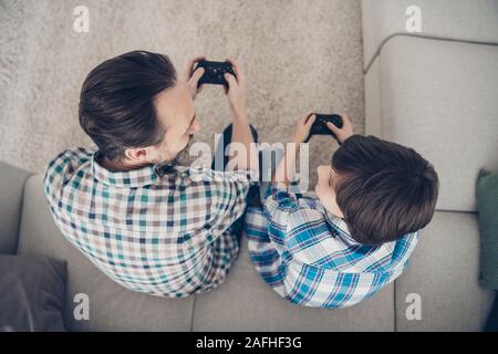 Top above high angle view portrait of two nice attractive guys dad and pre-teen son sitting on couch enjoying playing video game pad spending spare Stock Photo