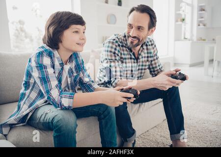 Profile side view portrait of two nice cheerful guys dad and pre-teen son sitting on sofa enjoying playing online game spending spare time at light Stock Photo