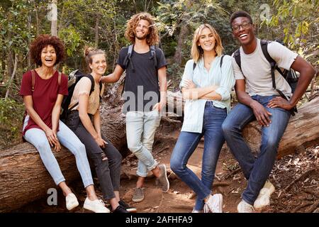 Young adult friends hiking in a forest resting on a fallen tree, smiling to camera, full length Stock Photo