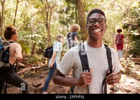 Waist up portrait of smiling millennial African American man hiking in a forest with friends, close up Stock Photo