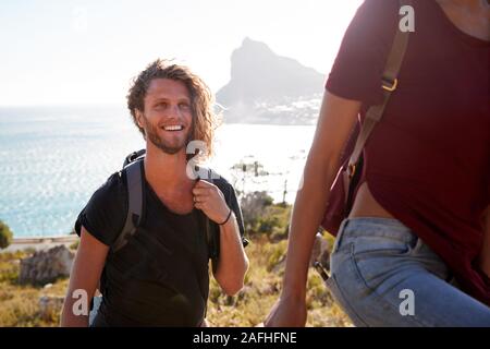 Young adult white man hiking with friends in countryside by the coast, smiling to camera, close up Stock Photo