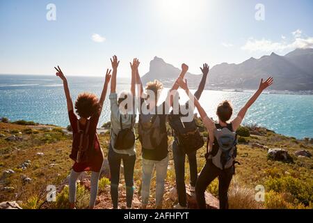 Millennial friends on a hiking trip celebrate reaching the summit and admire the view, back view Stock Photo
