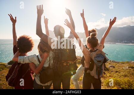 Millennial friends on a hiking trip celebrate reaching the summit and admire the view, back view Stock Photo