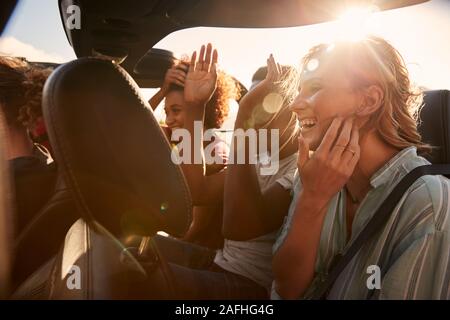 Happy young adult friends on a road trip vacation travelling in the back of an open car Stock Photo