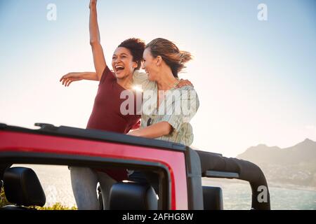 Two millennial female friends on a road trip standing in the back of an open top car, close up Stock Photo
