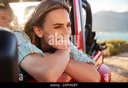 Millennial white woman on a road trip with friends leaning on car door enjoying view, close up Stock Photo
