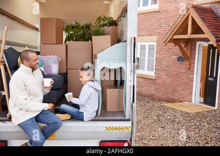 Father And Son Sitting On Tailgate Of Removal Truck Having Drink On Moving Day Stock Photo