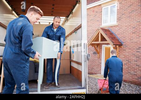 Removal Company Workers Unloading Furniture And Boxes From Truck Into New Home On Moving Day Stock Photo