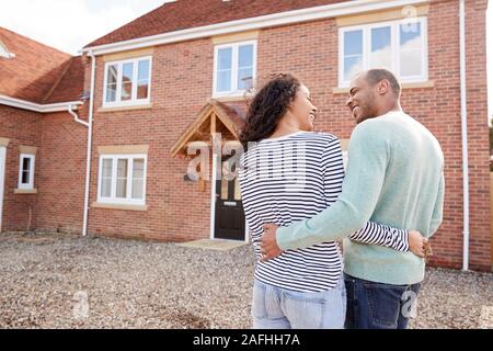 Rear View Of Couple Standing Outside New Home On Moving Day Looking At House Stock Photo