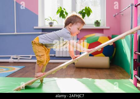 the little kid climbs up a wooden plate in the gym Stock Photo