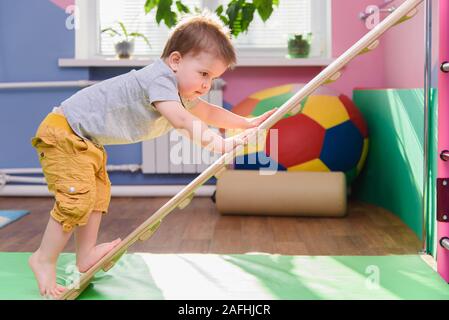 the little kid climbs up a wooden plate in the gym Stock Photo