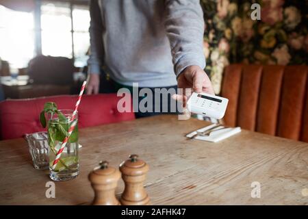 Close Up Of Waiter In Restaurant Holding Out Contactless Card Reader To Customer Stock Photo