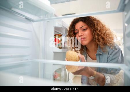 Disappointed Woman Looking Inside Refrigerator Empty Except For Potato On Shelf Stock Photo
