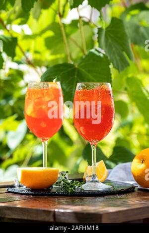 Two Aperol spritz cocktail in big wine glass with oranges, summer Italian fresh alcohol cold drink. Sunny garden with vineyard background Stock Photo