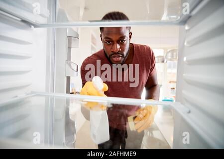 View Looking Out From Inside Empty Refrigerator As Man Wearing Rubber Gloves Cleans Shelves Stock Photo