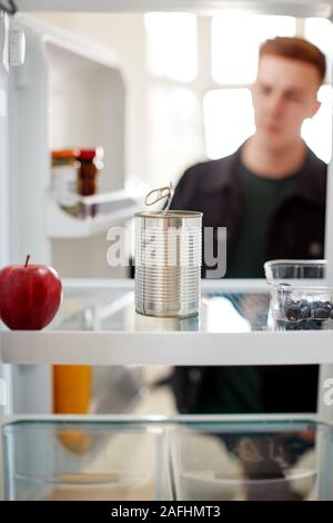 Young Man Looking Inside Refrigerator Empty Except For Open Tin Can On Shelf Stock Photo
