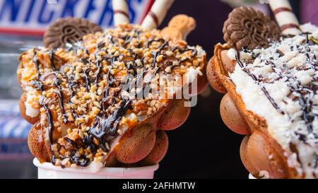 Bubble waffles with raspberries, chocolate and marshmallow in white paper cups are sold on Open kitchen food festival event. Hong kong waffles. Concep Stock Photo