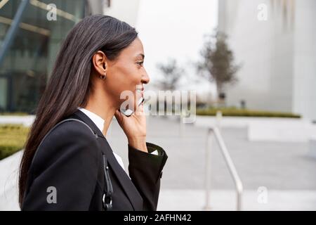 Businesswoman Commuting To Work Talking On Mobile Phone Outside Modern Office Building Stock Photo