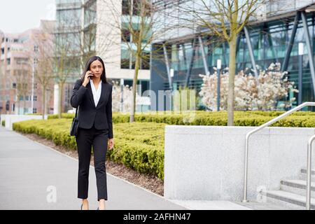 Businesswoman Commuting To Work Talking On Mobile Phone Outside Modern Office Building Stock Photo