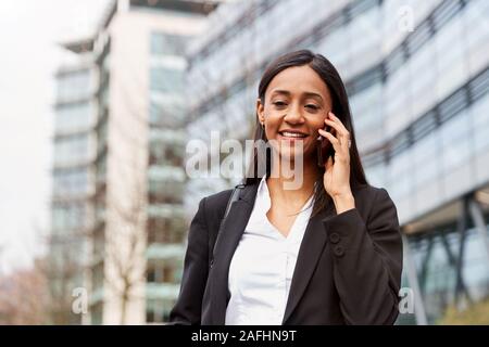 Businesswoman Commuting To Work Talking On Mobile Phone Outside Modern Office Building Stock Photo