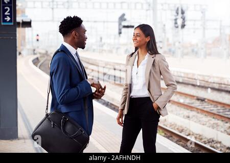 Businessman And Businesswoman Commuting To Work Talking On Railway Platform Waiting For Train Stock Photo