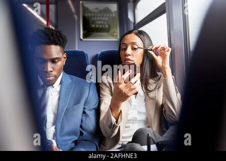 Businesswoman Sitting In Train Commuting To Work Putting On Make Up Stock Photo