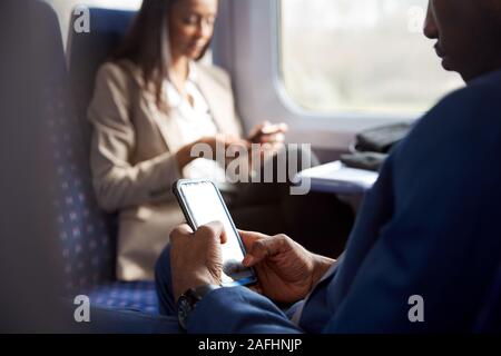 Close Up Of Business Passengers Sitting In Train Commuting To Work Looking At Mobile Phones Stock Photo