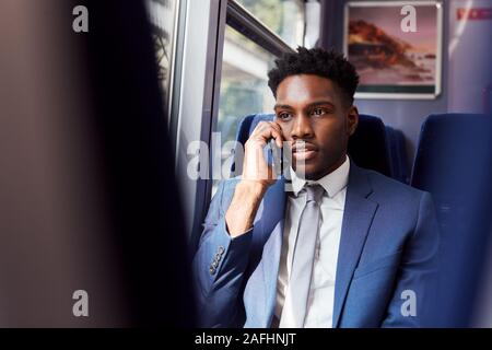 Businessman Sitting In Train Commuting To Work Making Call On Mobile Phone Stock Photo