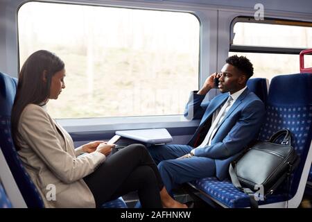 Business Passengers Sitting In Train Commuting To Work Using Mobile Phones Stock Photo