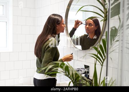 Businesswoman At Home Putting On Make Up In Mirror Before Leaving For Work Stock Photo