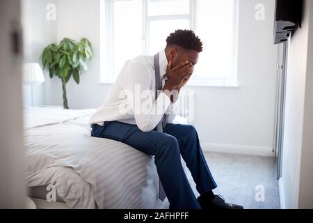 Stressed Businessman With Head In Hands Sitting On Edge Of Bed At Home Stock Photo