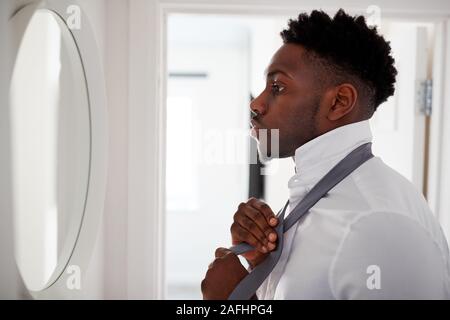 Businessman At Home Tying Necktie In Mirror Before Leaving For Work Stock Photo