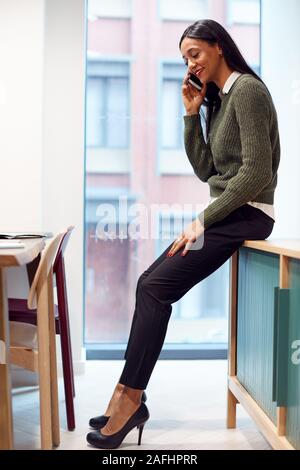 Businesswoman Sitting On Desk In Meeting Room Talking On Mobile Phone Stock Photo