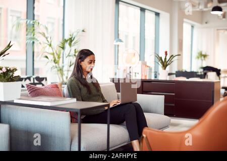 Businesswoman Sitting On Sofa Working On Laptop At Desk In Shared Workspace Office Stock Photo