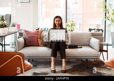 Portrait Of Businesswoman Sitting On Sofa Working On Laptop At Desk In Shared Workspace Office Stock Photo