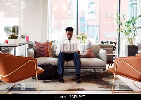 Businessman Sitting On Sofa Working On Laptop At Desk In Shared Workspace Office Stock Photo