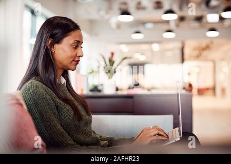 Businesswoman Sitting On Sofa Working On Laptop At Desk In Shared Workspace Office Stock Photo