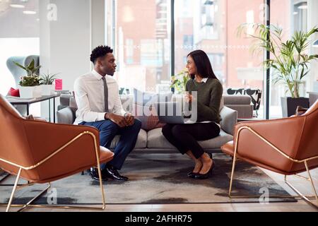 Businesswoman Interviewing Male Job Candidate In Seating Area Of Modern Office Stock Photo
