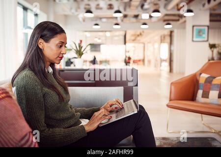 Businesswoman Sitting On Sofa Working On Laptop At Desk In Shared Workspace Office Stock Photo