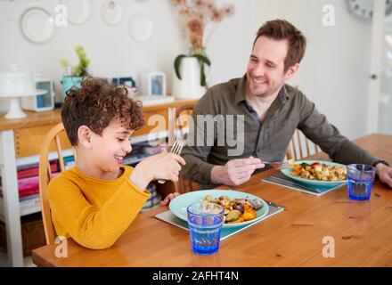 Single Father Sitting At Table Eating Meal With Son In Kitchen At Home Stock Photo