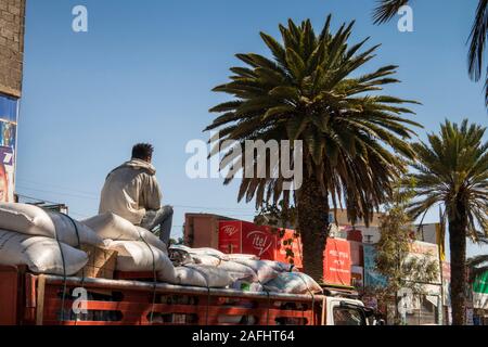 Ethiopia, Tigray, Mekele, city centre, Hahefen St, man sat on top of sack-laden truck passing shops Stock Photo