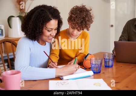 Mother Helping Son With Homework On Kitchen Table At Home Stock Photo