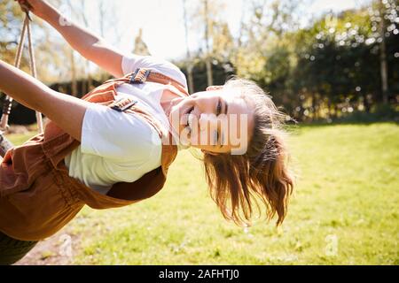 Portrait Of Girl Having Fun On Tyre Swing In Garden At Home Stock Photo