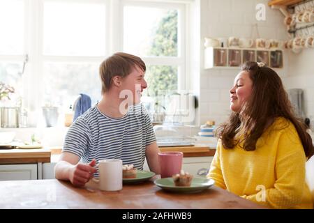 Young Downs Syndrome Couple Enjoying Tea And Cake In Kitchen At Home Stock Photo