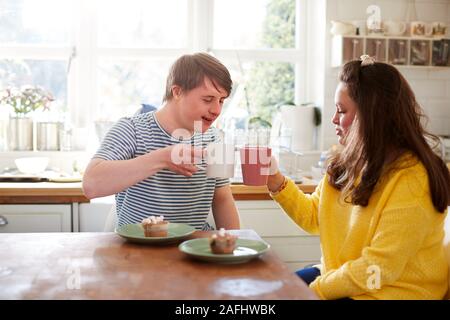 Young Downs Syndrome Couple Enjoying Tea And Cake In Kitchen At Home Stock Photo