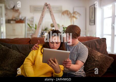 Young Downs Syndrome Couple Sitting On Sofa Using Digital Tablet At Home Stock Photo